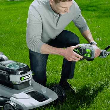 Man swapping EGO battery from EGO lawn mower to EGO string trimmer.